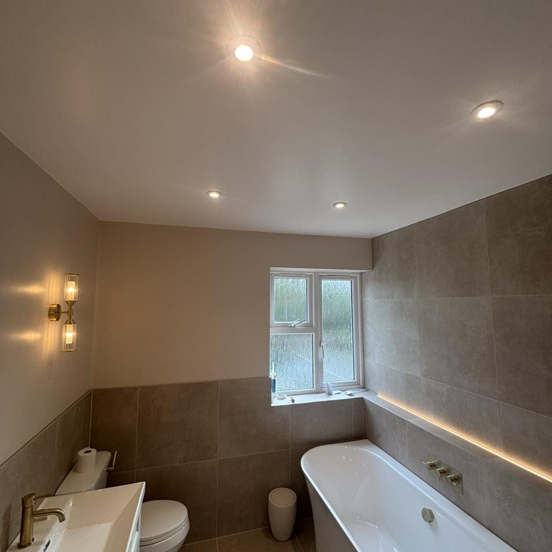 Modern bathroom featuring a bathtub, sink, and large window with subtle lighting.